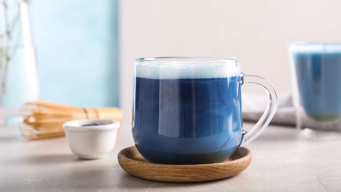 Butterfly Pea Flower matcha in a clear mug in a wooden coaster with a blurred white kitchen background