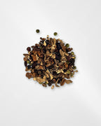 A small pile of loose dried botanical tea or spice blend with brown leaves, dark berries, and a few green round pieces, photographed on a clean white background.