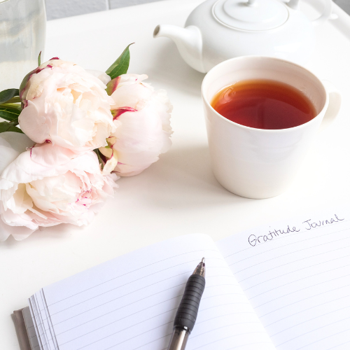 Image of cosmic chai tea brewed in a white mug next to open notebook and flowers with white background