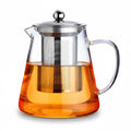 Clear glass teapot with a stainless steel mesh infuser and lid, filled with amber tea, on a white background.