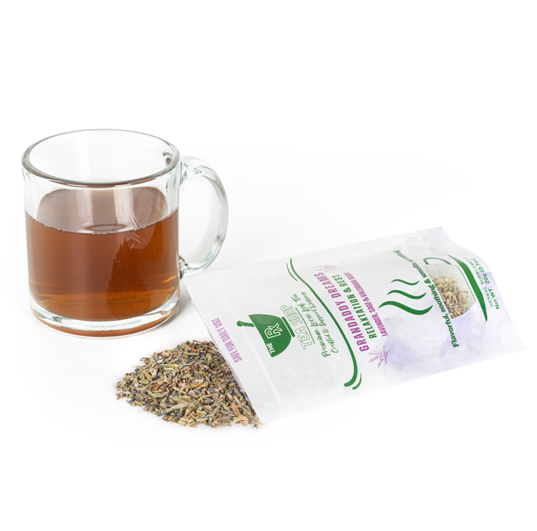 Herbs spilling out of a bag of Grandaddy Dreams next to clear mug with dark colored tea on a white background