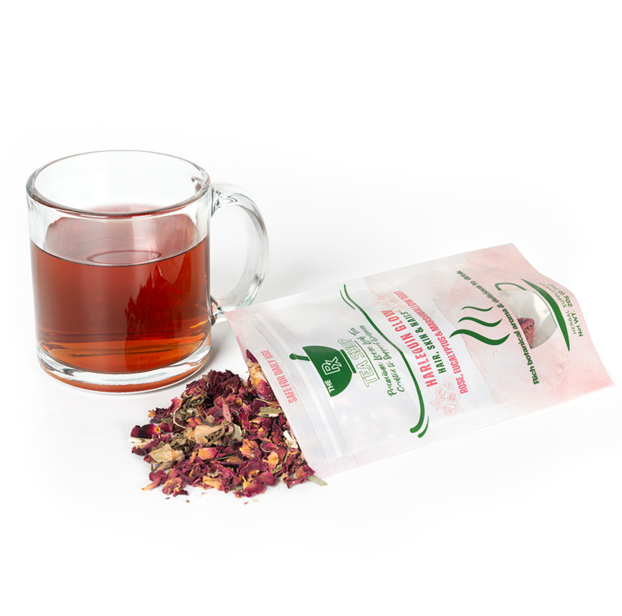 Dried rose petals and herbs spilling out of a bag of Harlequin Glow next to a clear mug filled with dark colored tea on a white background 
