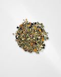 A small pile of loose-leaf herbal tea blend containing dried green, brown, orange, and black botanical pieces, centered on a plain light gray background.