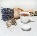 Image of lavender stock and tea infuser next to tea in porcelain teacup on white background