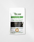 A stand-up pouch of Moroccan Mint Green Tea Blend by The Tea Shop, featuring a white package with green and black text and a clear window showing loose leaf tea inside, set against a light gray background.