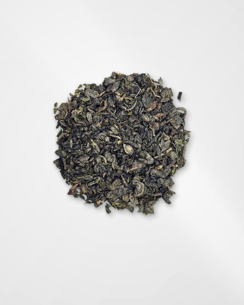 A small mound of loose-leaf tea leaves, appearing dark green to black with subtle olive and brownish highlights, photographed from above on a plain white background.