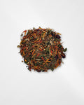 A small pile of loose-leaf herbal tea blend containing dried flowers, leaves, and roots in earthy brown, orange, green, and purple tones, centered on a plain white background.