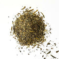 A small pile of loose dried green tea leaves on a plain white background.