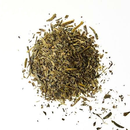 A small pile of loose dried green tea leaves on a plain white background.