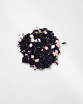 A small pile of loose-leaf tea blend on a plain white background, featuring dark tea leaves mixed with small pink pieces of air dried peach.