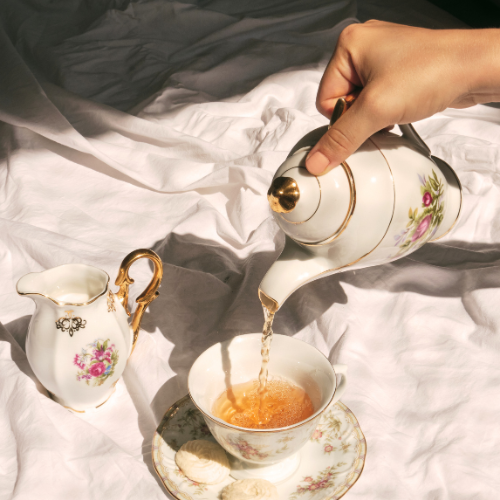 Image of someone pouring tea into porcelain cup from porcelain teapot on white sheet