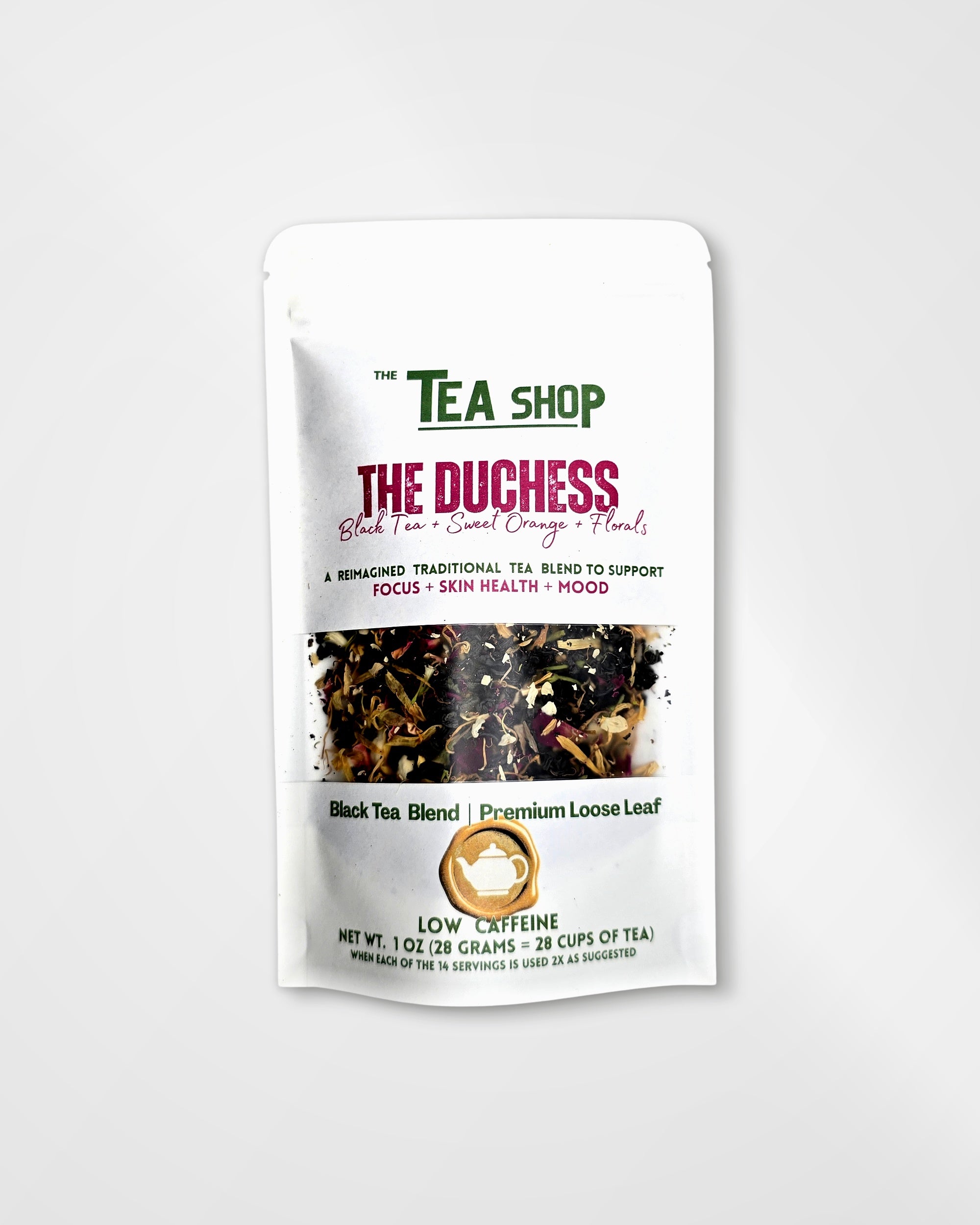 A stand-up pouch of loose leaf tea from 'The Tea Shop' on a light gray background. The packaging is white with green and magenta text, featuring a clear window that displays the dark brown and black loose leaf tea blend inside.