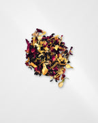 A small pile of loose-leaf herbal tea blend containing dried rose petals, yellow flower pieces, and dark tea leaves, photographed on a clean white background.