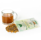 A pile of dried yellow and green herbal tea leaves with rosemary pieces spilling out of a bag of Yellow Hybrid tea next to a clear glass mug with amber colored tea on a white background 