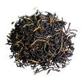 A pile of loose-leaf tea leaves, predominantly dark brown to black with visible golden-yellow tips, isolated on a solid white background.