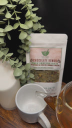 Short video clip of Chocolate venus tea being poured into white mug from clear teapot with green scenery 