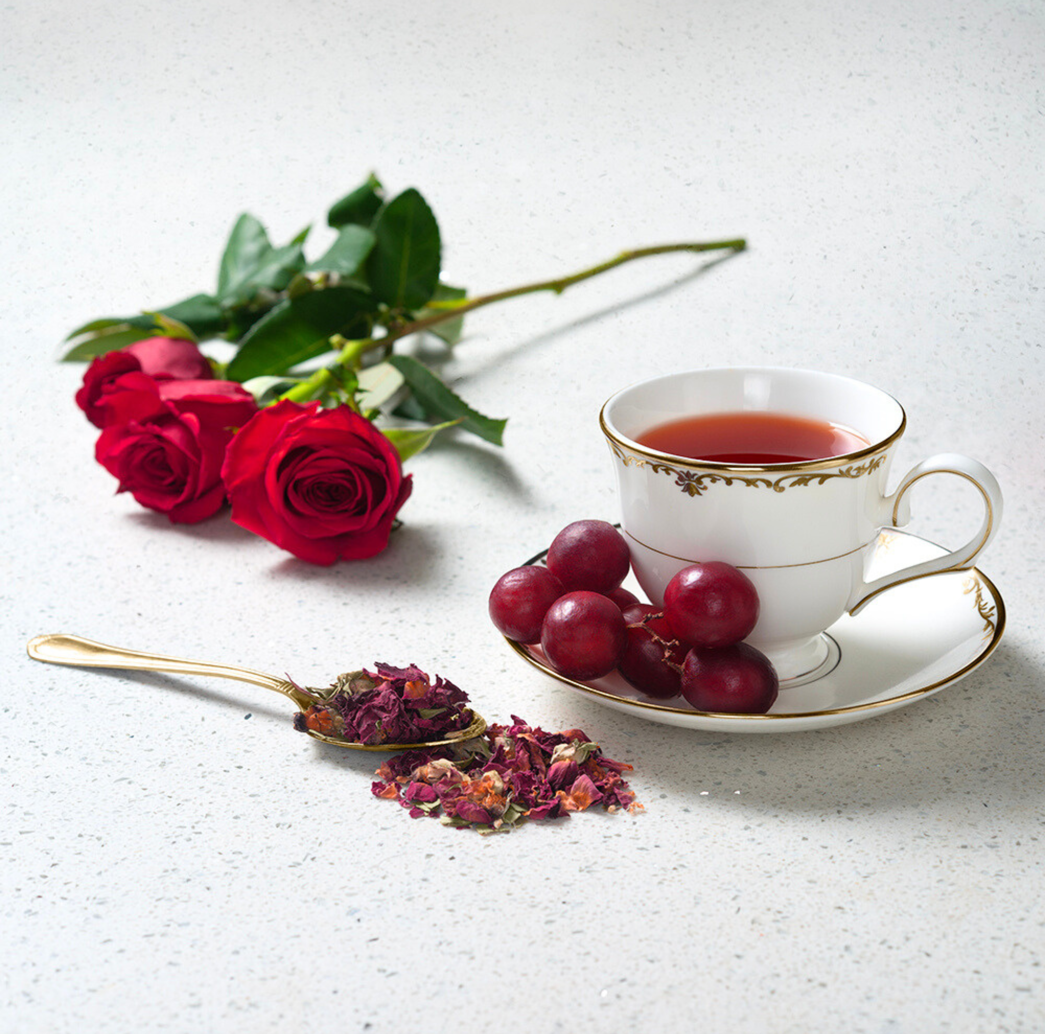 Red rose and stem next to porcelain teacup on white background